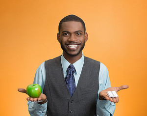 Portrait young, fit, happy executive man holding green fresh apple in one hand, pills, vitamins in another. Sugar free chewing gum, dentist recommended. Face expressions, emotion, health care. Dieting